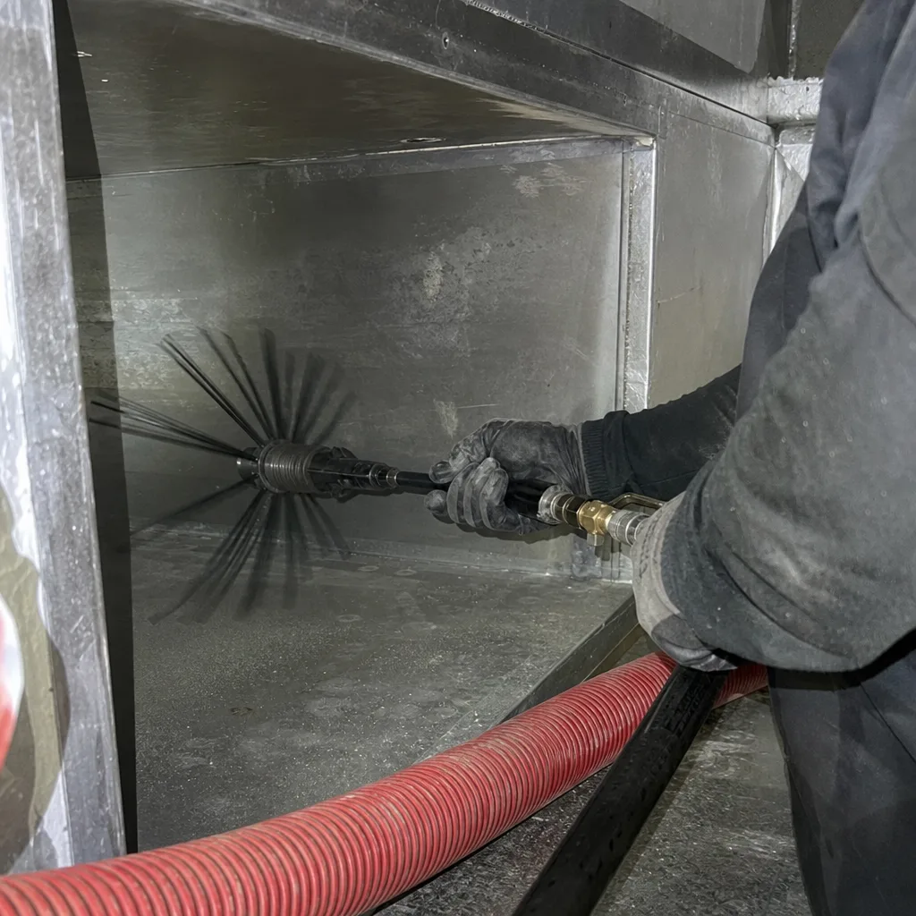 Technician using a rotating brush tool for professional air duct cleaning
